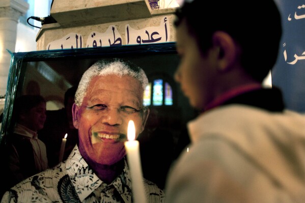 A Palestinian child holds a lit candle as he prays in front of a poster of late South African leader Nelson Mandela, during a special service in his honor at the Holy Family Church, in the West Bank city of Ramallah, Sunday, Dec. 8, 2013.  (AP Photo/Nasser Nasser, File)