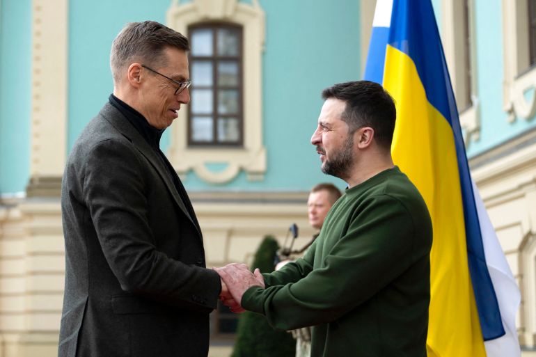 FInland's President Alexander Stubb meeting Ukrainian President Volodymyr Zelenskyy in Kyiv. Zelenskyy is welcoming him and they are shaking hands. A Ukrainian flag is behind them.